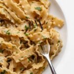 White plate with anchovy pasta wrapped around a fork. Chopped parsley on top.