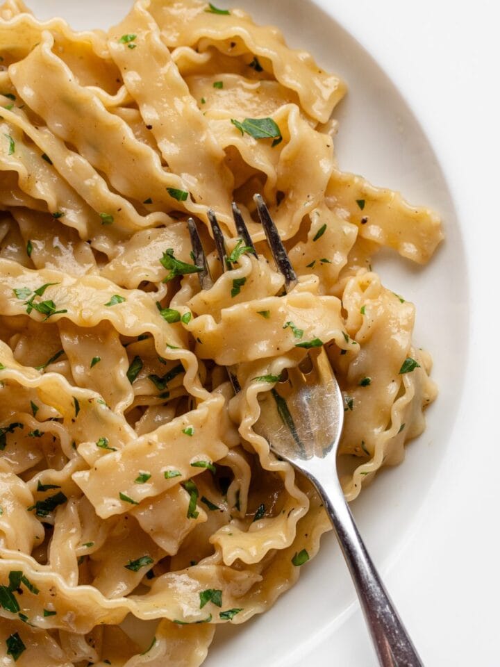 White plate with anchovy pasta wrapped around a fork. Chopped parsley on top.