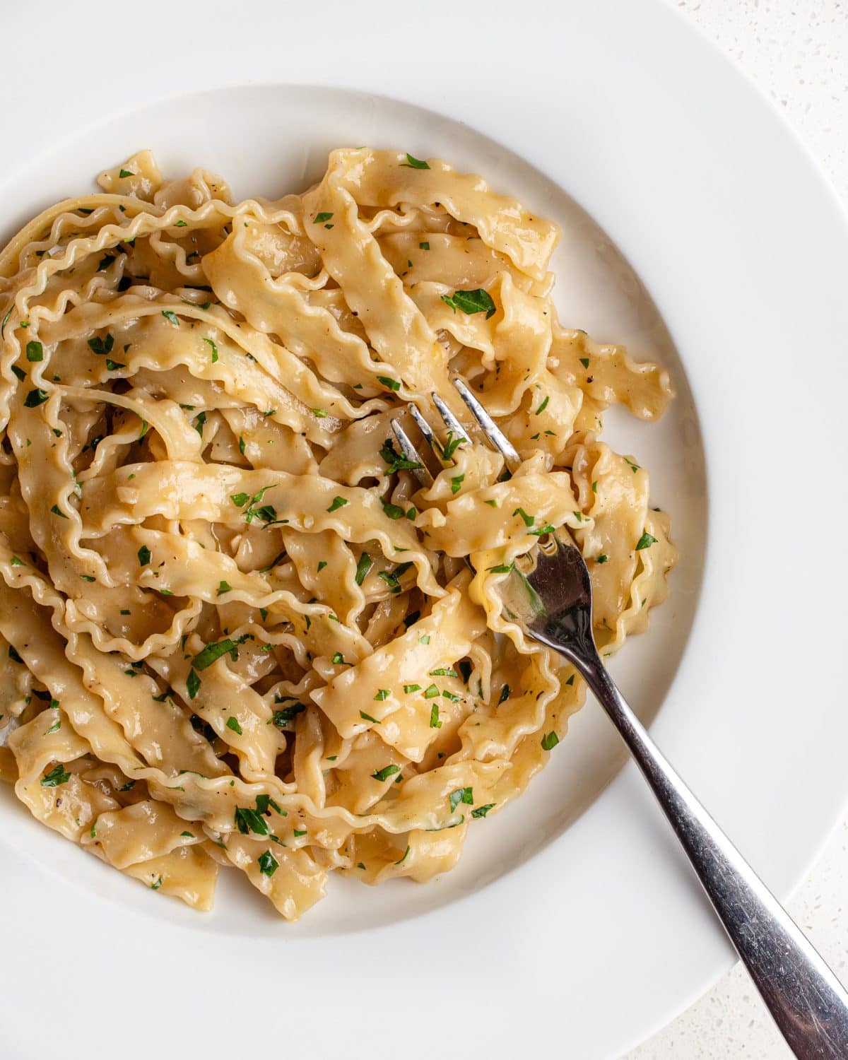 White plate with anchovy pasta wrapped around a fork. Chopped parsley on top.