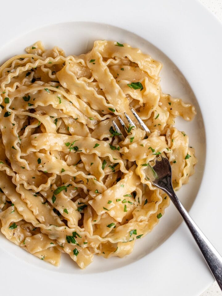 White plate with Malfadine pasta in an anchovy butter sauce. Parsley tossed through and a fork resting into the noodles.