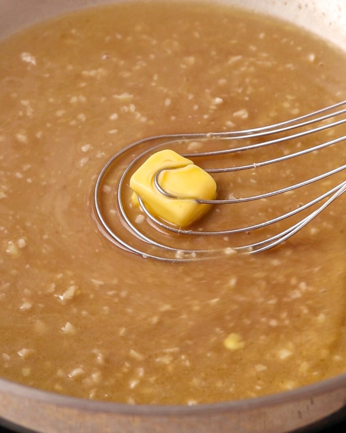 A whisk mixing a cube of butter into the pan.