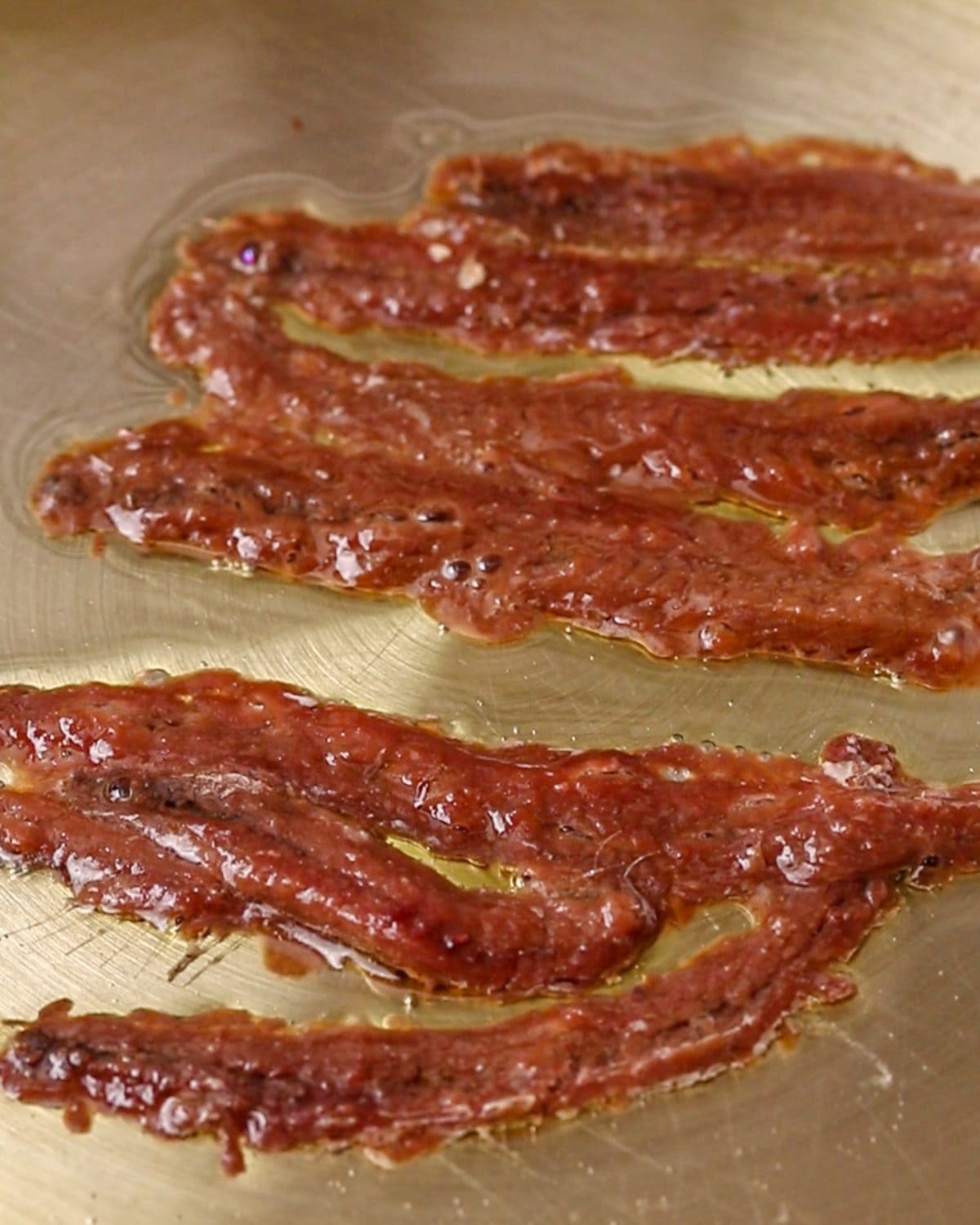 Anchovies sizzling in a stainless steel pan.