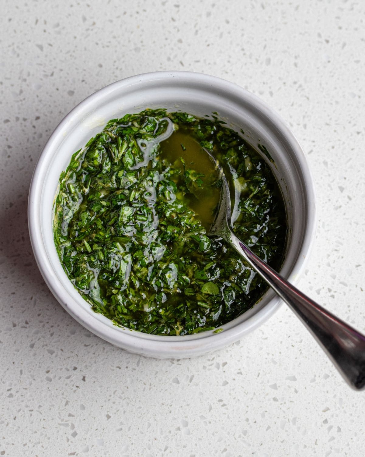 A white ramekin with gremolata and a teaspoon resting in.