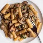 White plate with rigatoni in a sausage and mushroom sauce. Fork resting in.