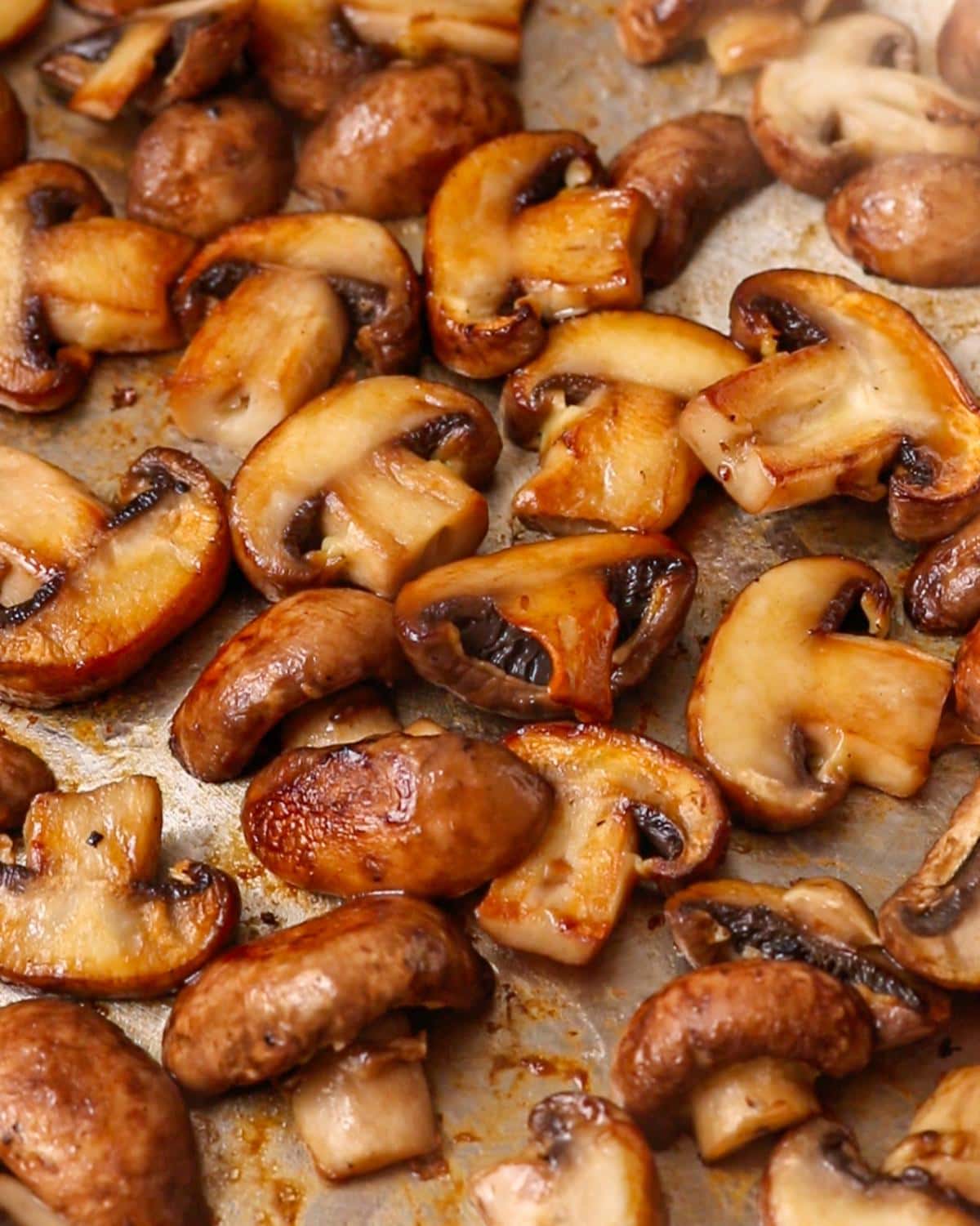 Sliced golden mushrooms sizzling in a stainless steel pan.