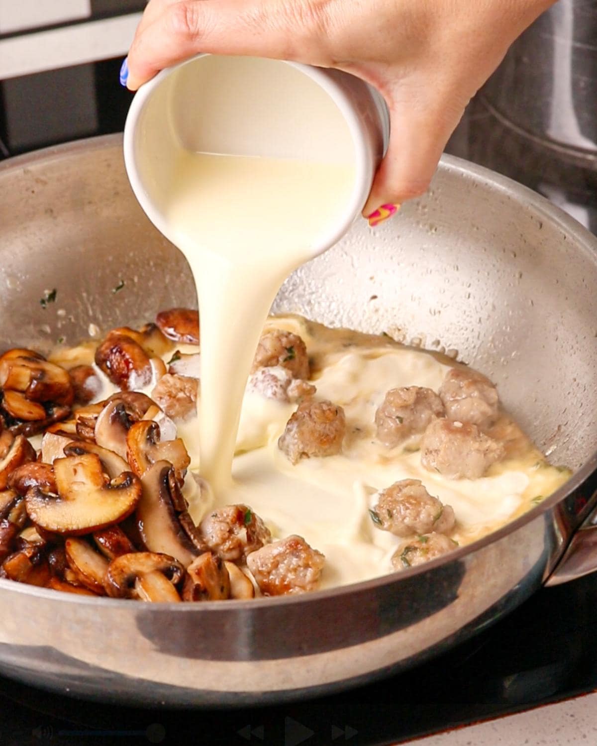 Hand pouring cream into the pan with mushrooms added back in.