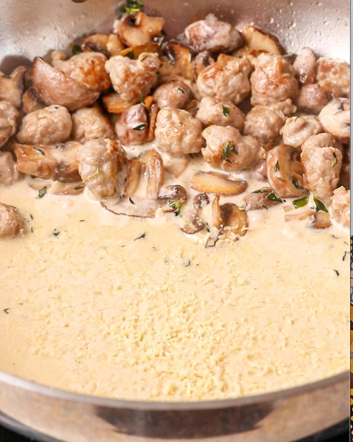 Sausage and mushrooms pushed to one side of pan with parmesan sprinkled on top of cream.