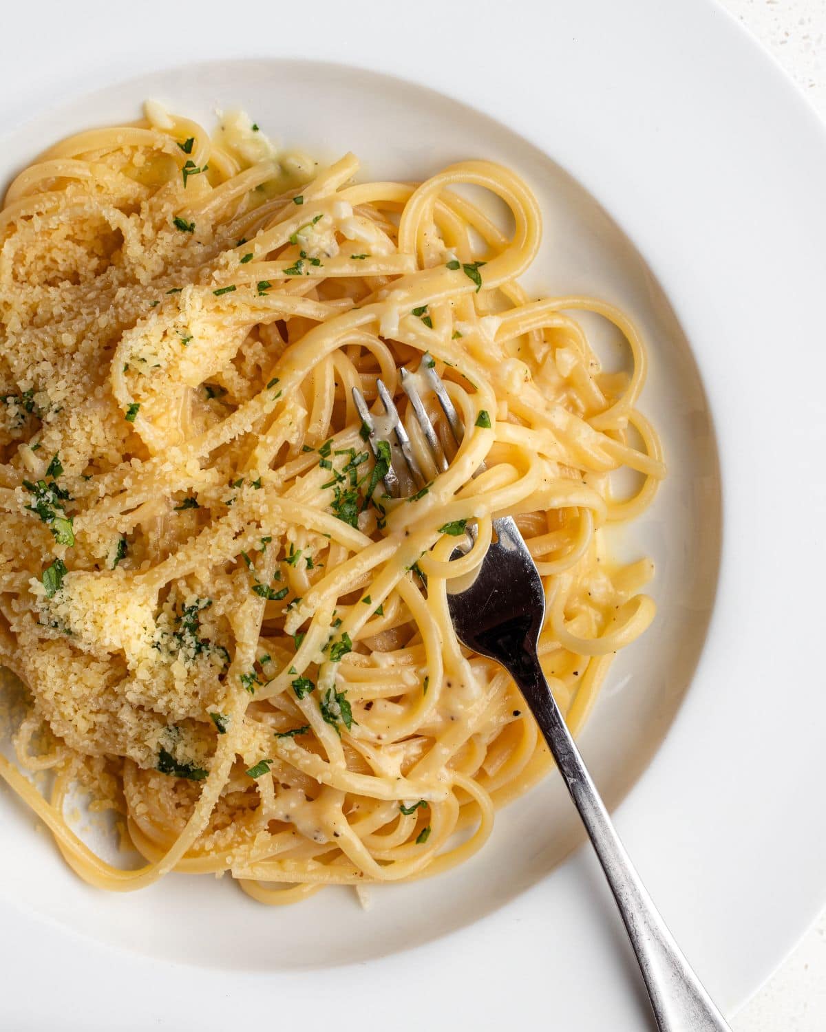 White plate with linguine in a garlic butter sauce. Fork resting in with noodles wrapped around.