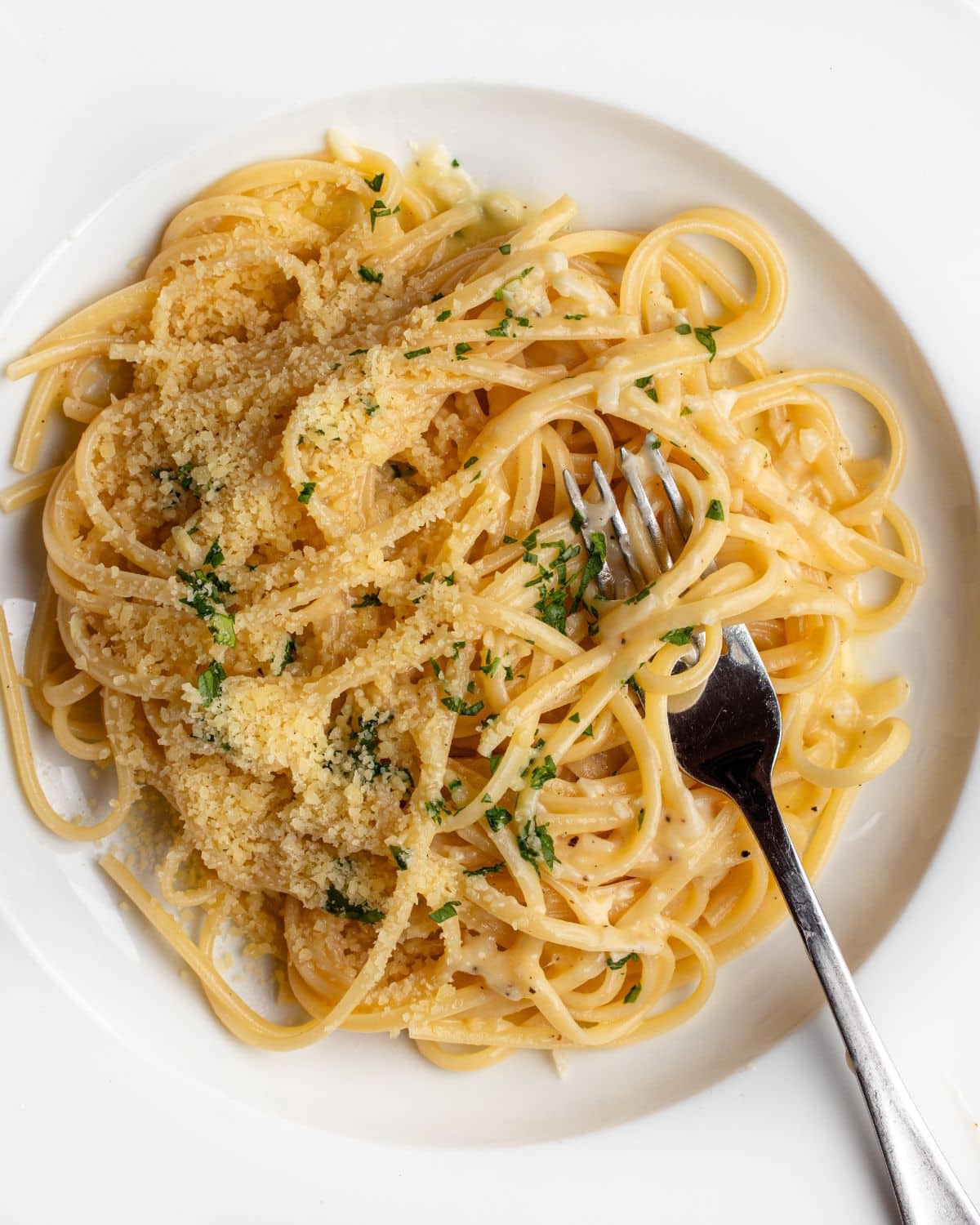 White plate with linguine in a garlic butter sauce. Fork resting in with noodles wrapped around