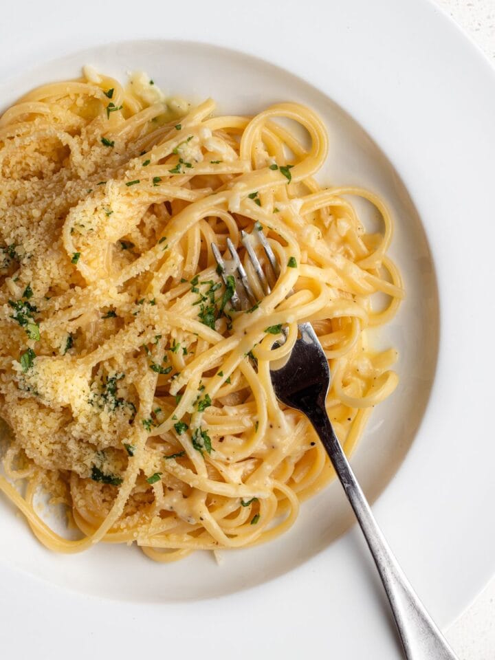 White plate with linguine in a garlic butter sauce. Fork resting in with noodles wrapped around.