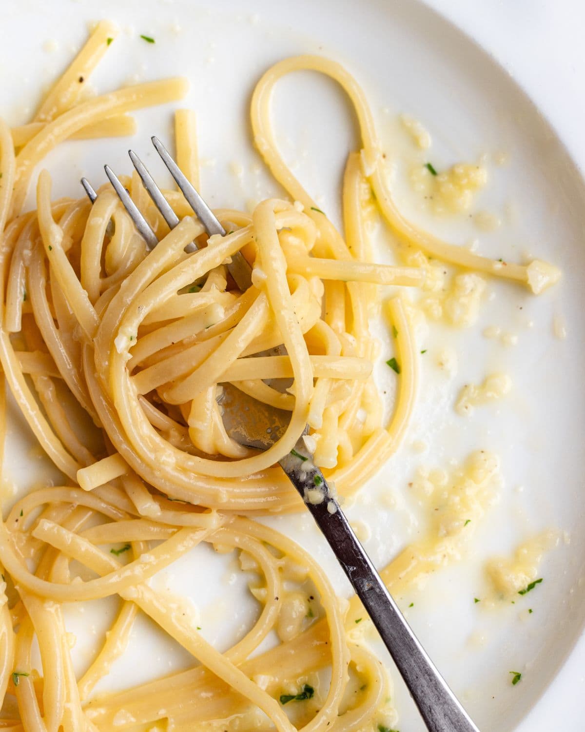 Linguine noodles wrapped around a fork with the garlic butter glossy on top.