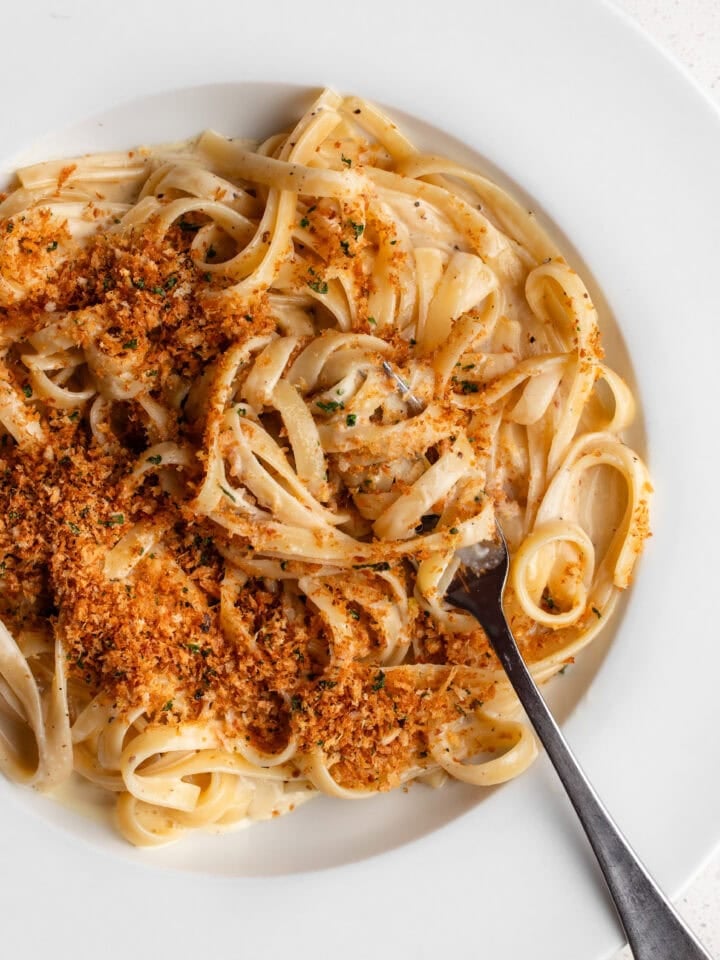 White plate with linguine in a creamy sauce and toasted panko pangrattato on top.