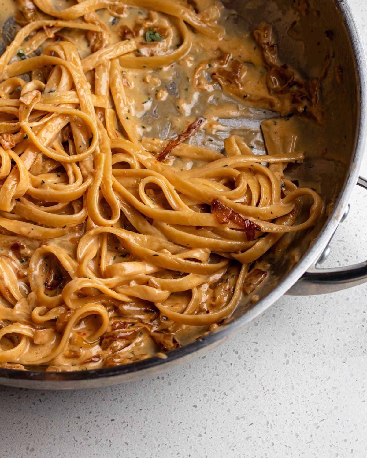Stainless steel pan with linguine in a creamy caramelized onion sauce.