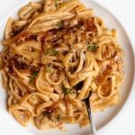 White plate with linguine in a creamy caramelized onion sauce. Fork resting onto plate.