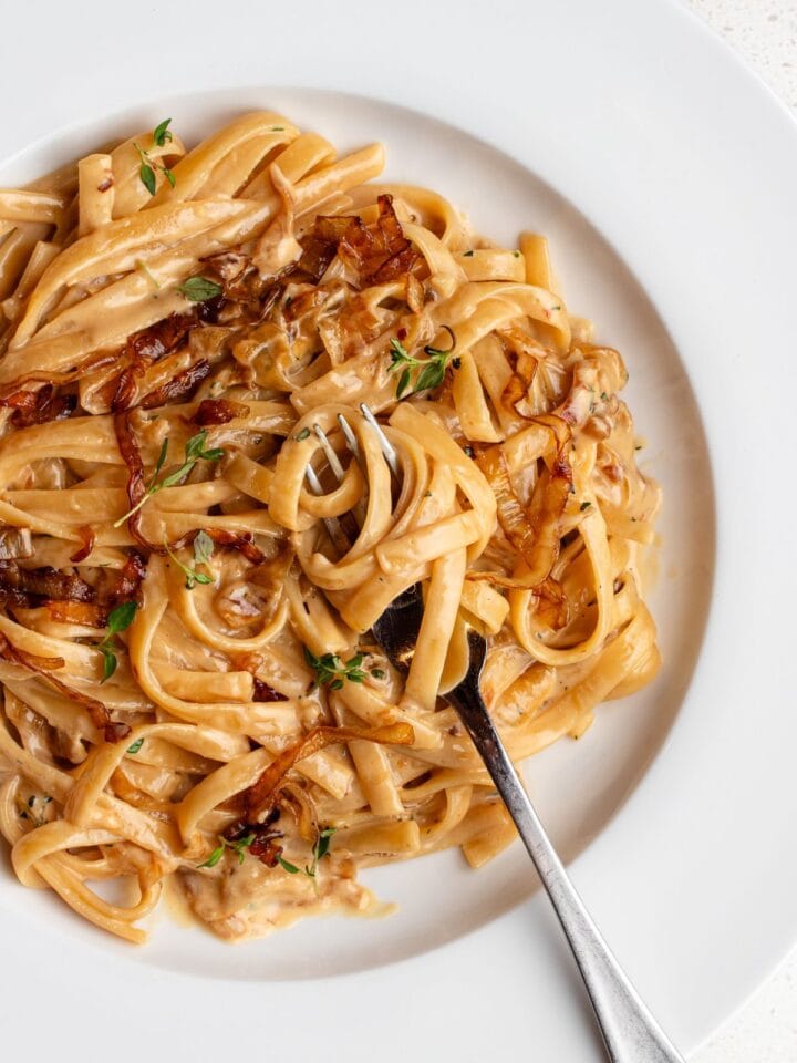 White plate with linguine in a creamy caramelized onion sauce. Fork resting onto plate.
