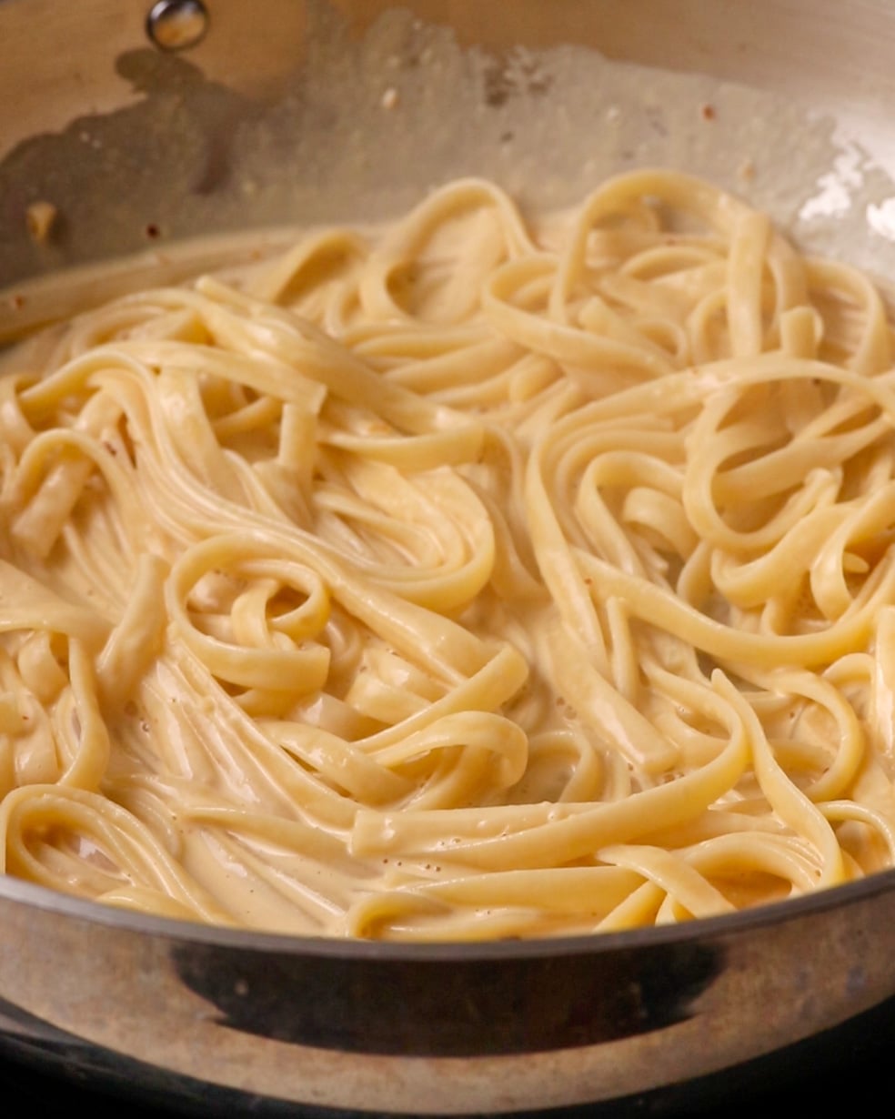 Cooked pasta being tossed through a creamy sauce with pasta water.