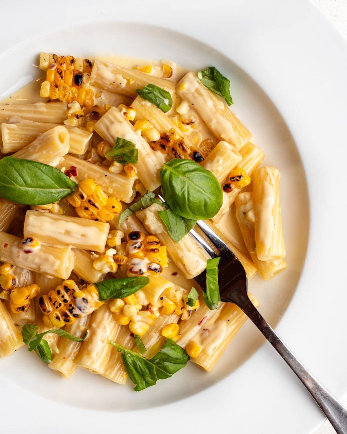 Rigatoni in a creamy sauce with charred corn and basil leaves mixed through.