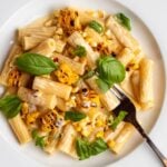 Rigatoni in a creamy sauce with charred corn and basil leaves mixed through.