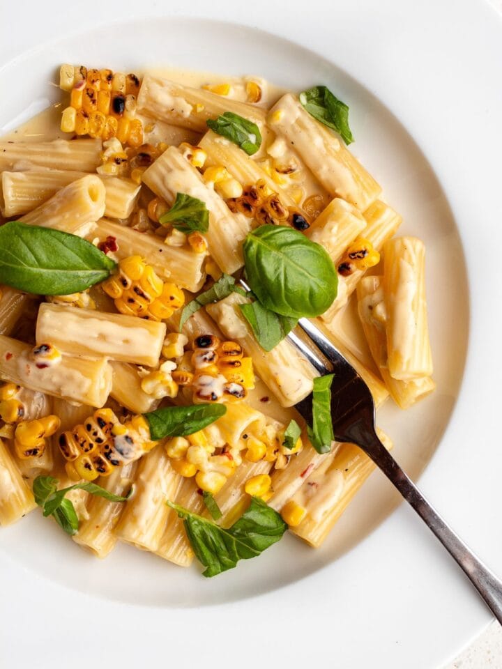 Rigatoni in a creamy sauce with charred corn and basil leaves mixed through.