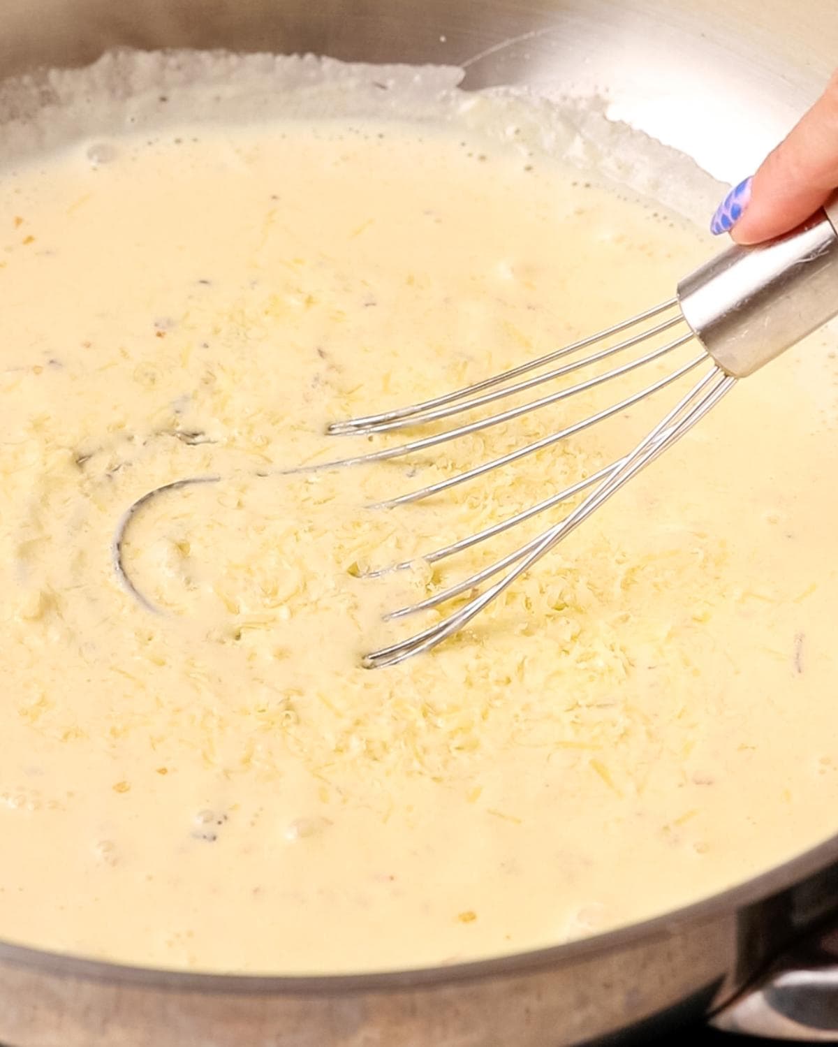 Finely grated parmesan melting into a creamy garlic sauce in a pan.