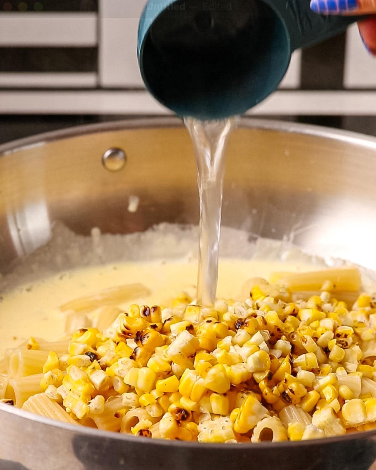 Cooked pasta and charred corn being mixed with creamy sauce and pasta water.