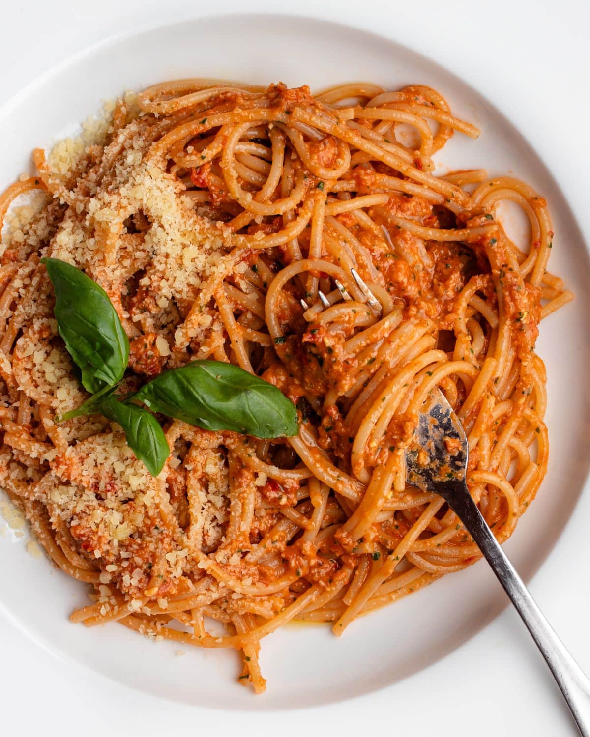 White plate with spaghetti in a sun-dried tomato pesto sauce. Fork resting with noodles wrapped around it.
