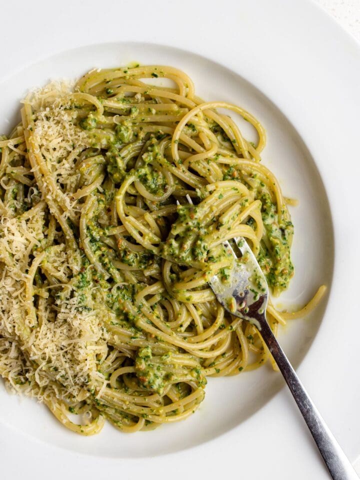 White plate with spaghetti in a pesto sauce. Fork resting into pasta.
