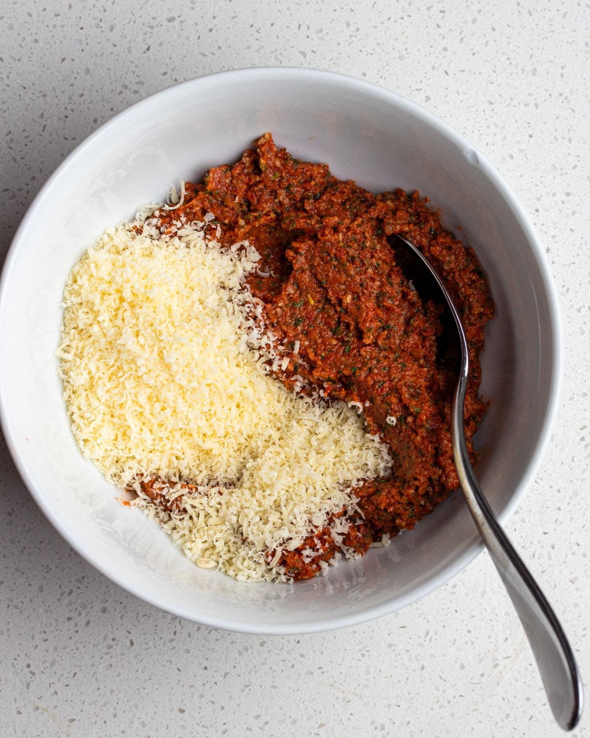 Sun-dried tomato pesto mixed with grated parmesan cheese in a bowl.