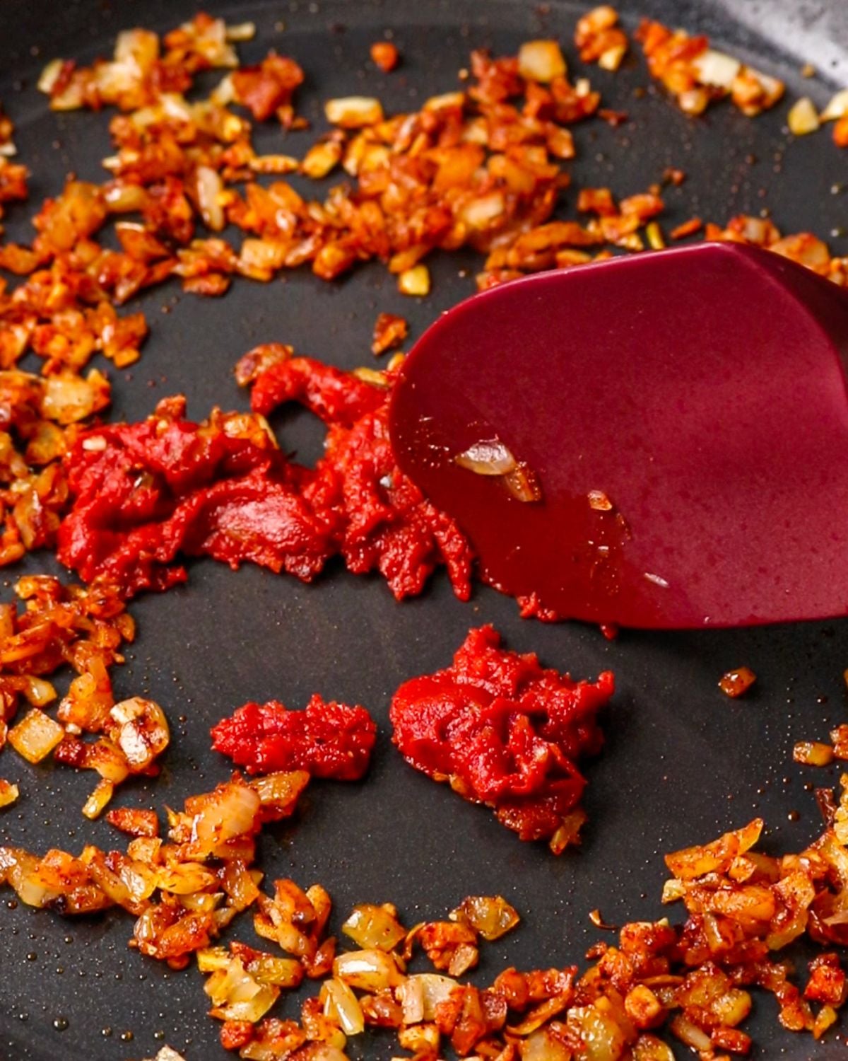 Tomato paste caramelizing in a skillet with onion and garlic.