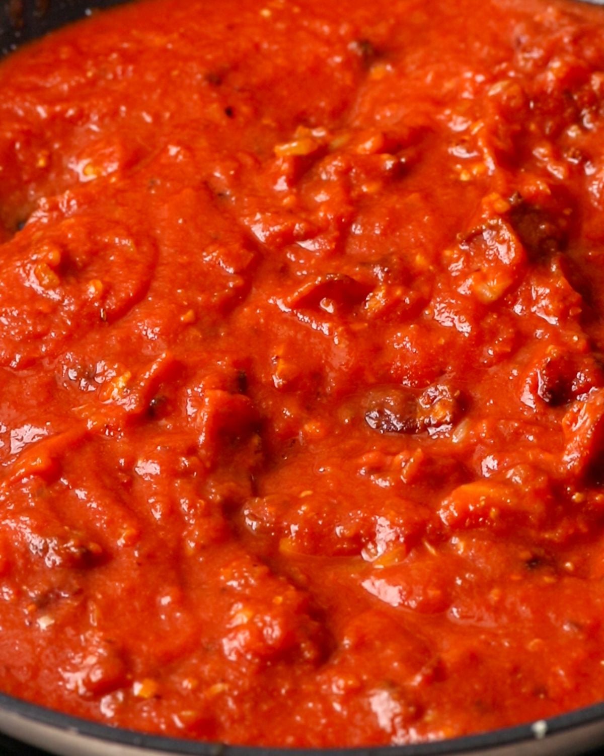 Tomato sauce simmering in a skillet with crispy bacon.