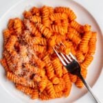 White plate with fusilli pasta in a roasted red pepper sauce. Fork resting into pasta.