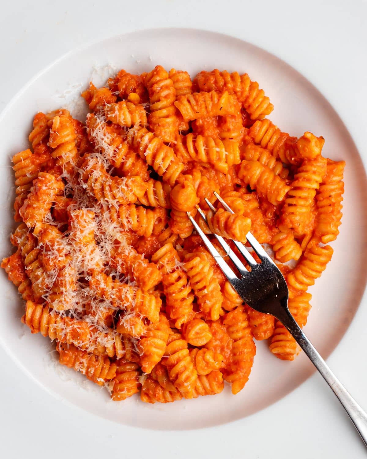 White plate with fusilli pasta in a roasted red pepper sauce. Fork resting into pasta.