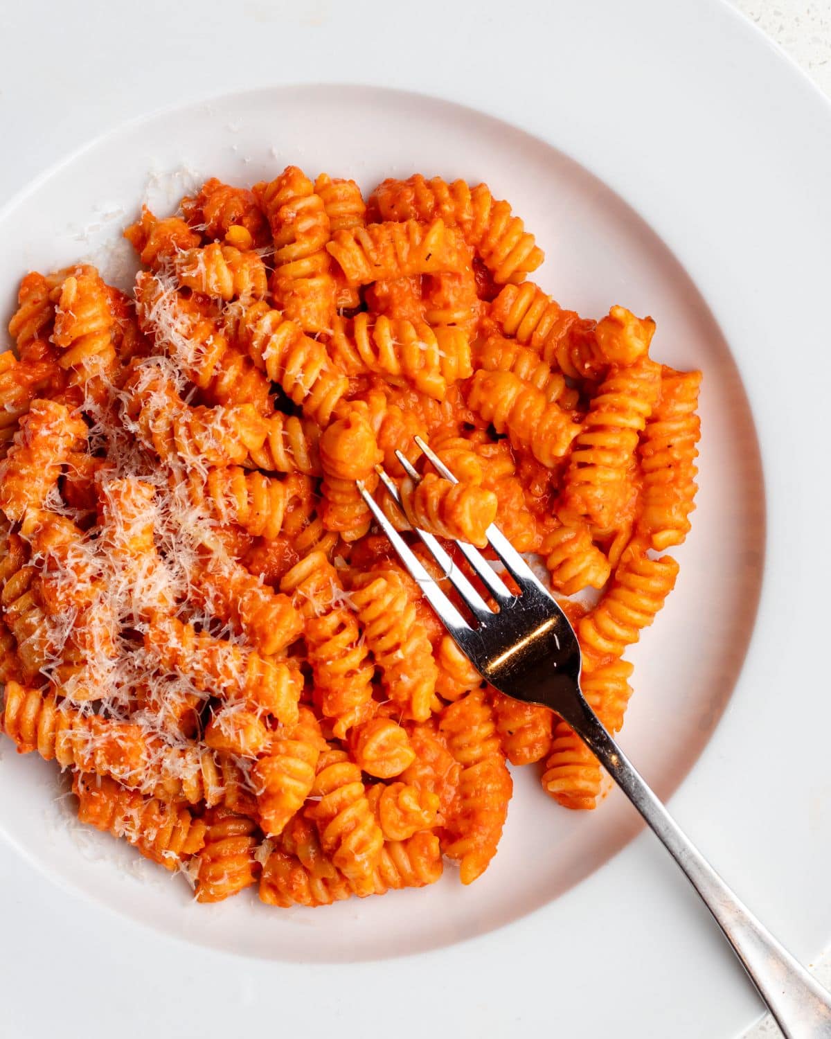 White plate with fusilli pasta in a roasted red pepper sauce. Fork resting into pasta.