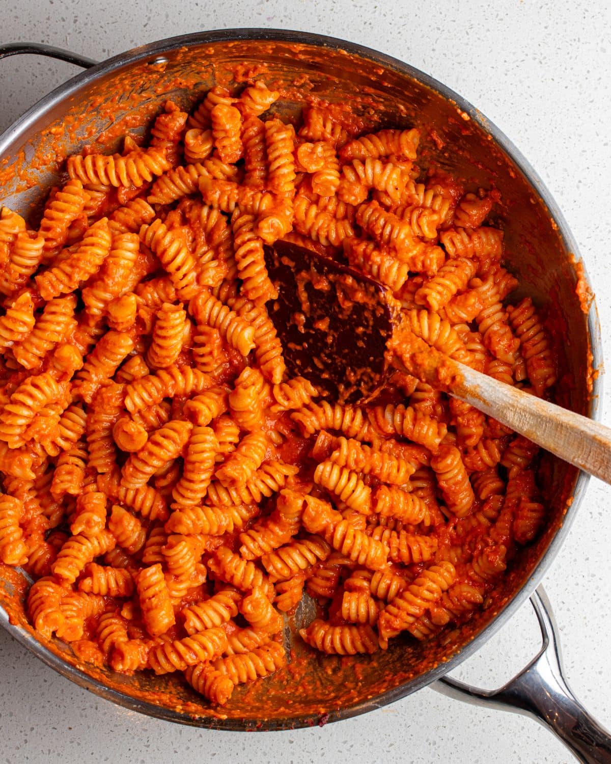 Frypan with roasted red pepper pasta and a spatula resting into pan.