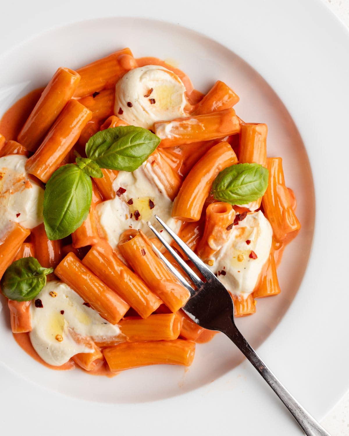 Dollops of whipped feta on a creamy tomato pasta. Fork resting onto plate.