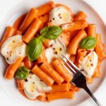 Dollops of whipped feta on a creamy tomato pasta. Fork resting onto plate.