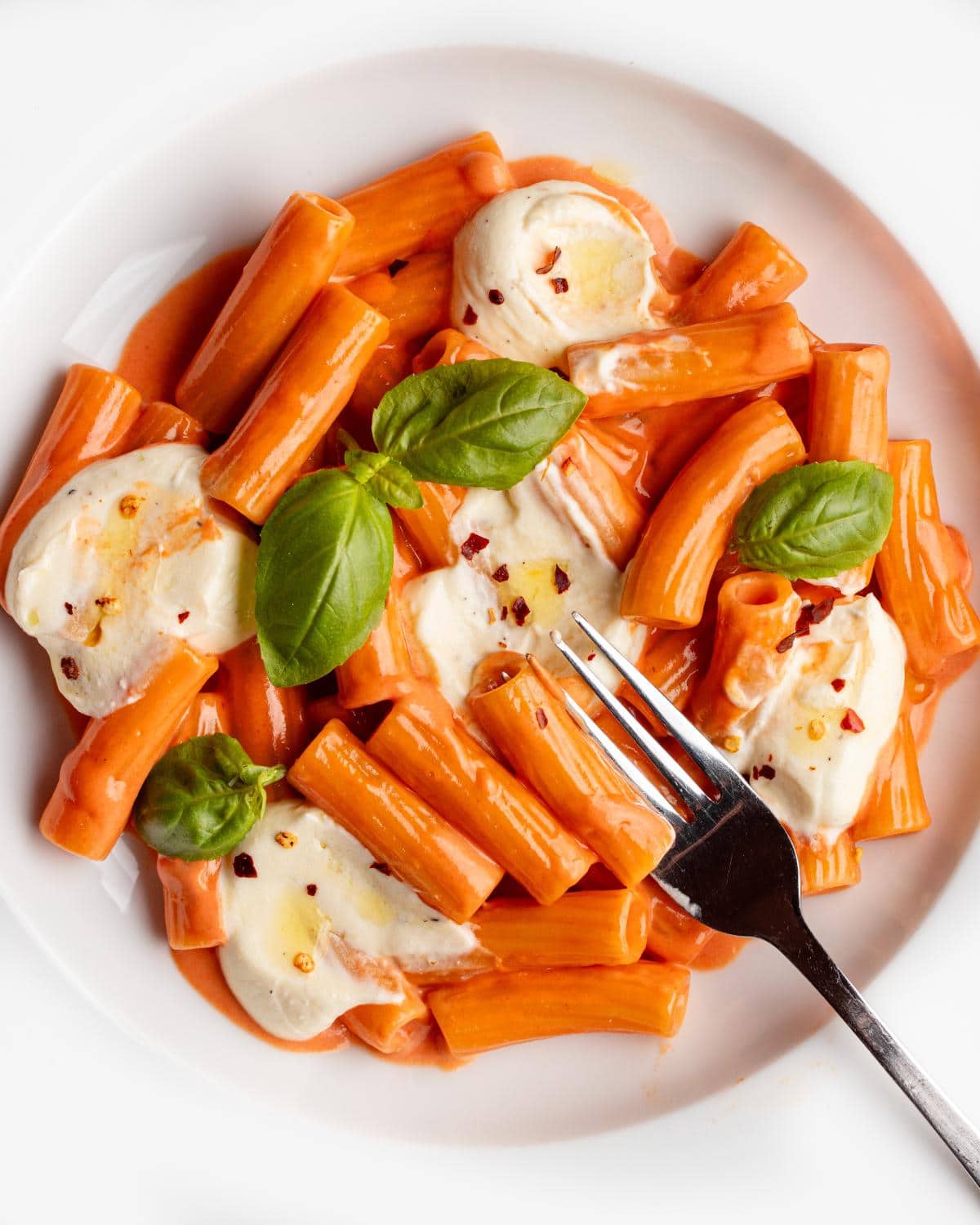 Dollops of whipped feta on a creamy tomato pasta. Fork resting onto plate.