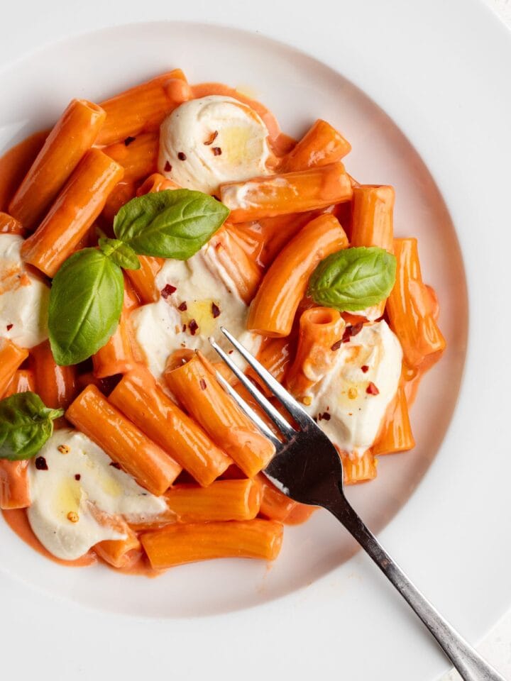 Dollops of whipped feta on a creamy tomato pasta. Fork resting onto plate.