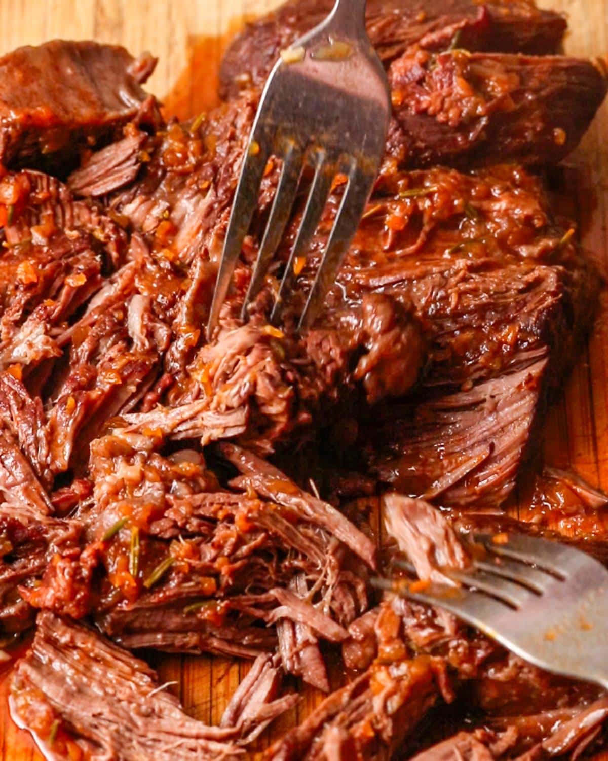 Tender beef chuck shredded with two forks after slow cooking.