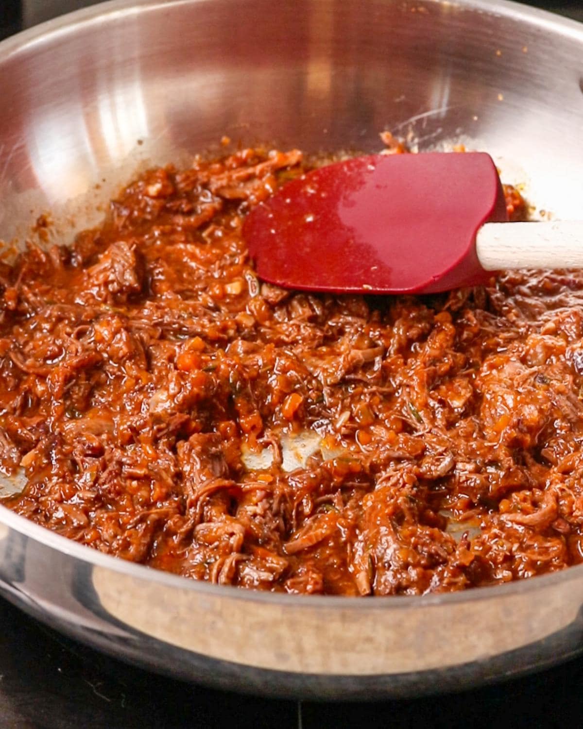 Beef ragu in a fry pan with spatula resting.