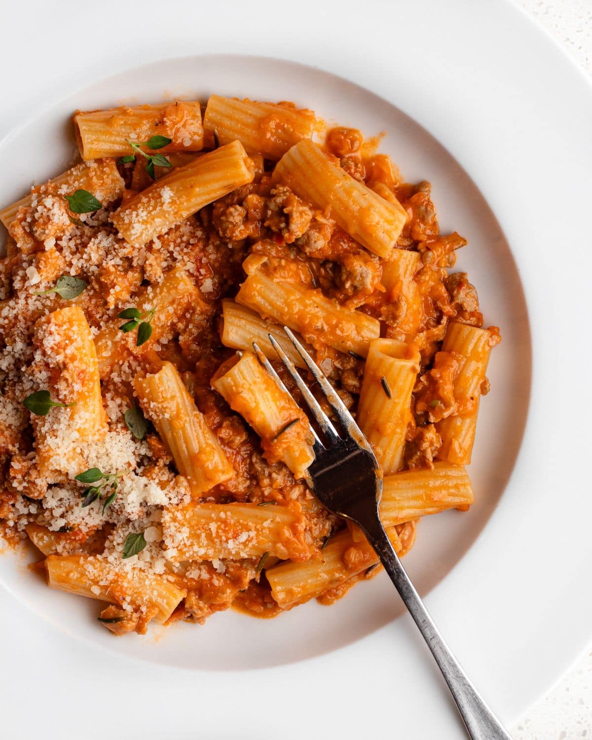 White plate with sausage ragu tossed through rigatoni. Fork resting in.