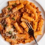 White plate with sausage ragu tossed through rigatoni. Fork resting in.