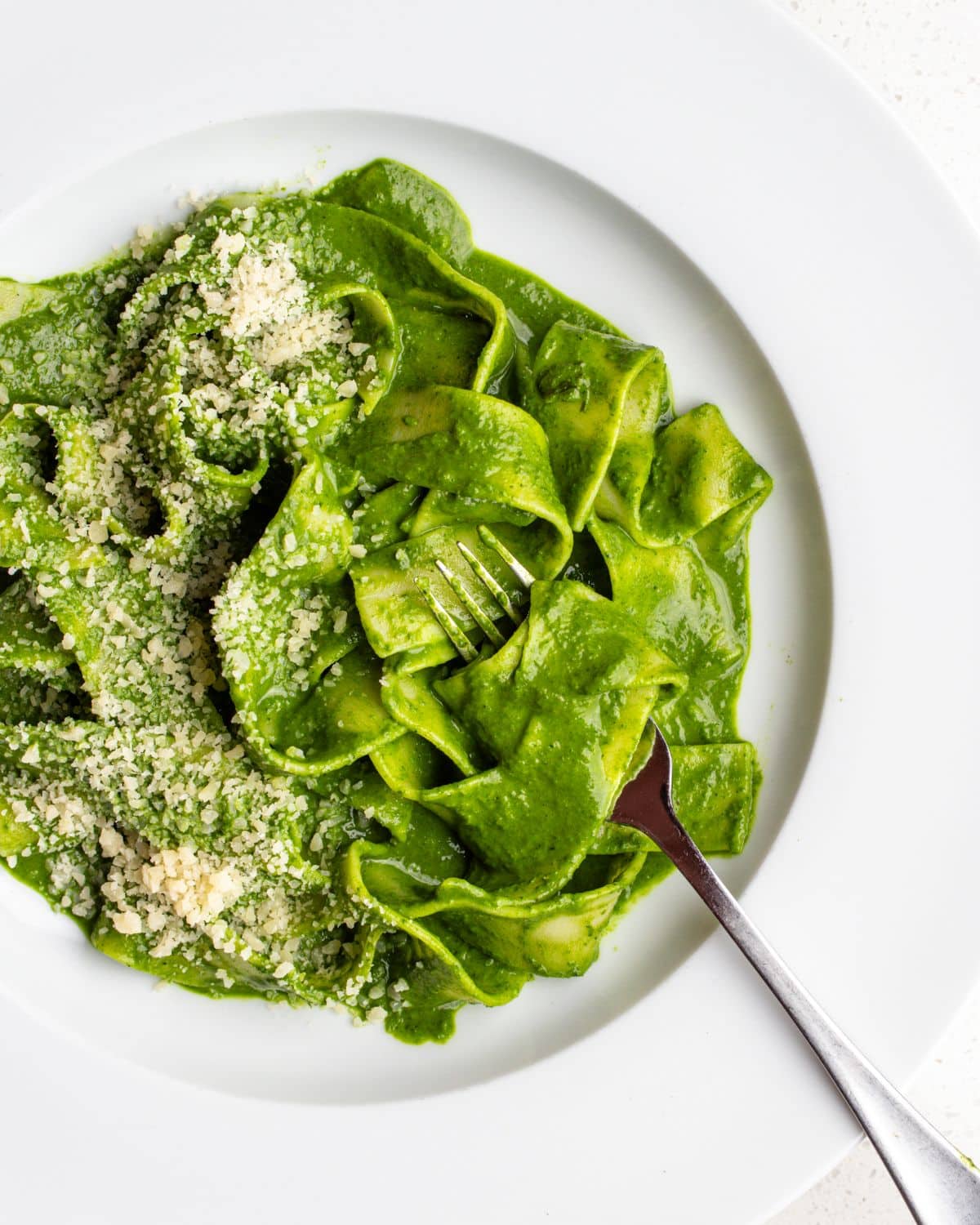 White plate with pappardelle pasta in a cavolo nero green sauce. Fork resting in.