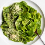White plate with pappardelle pasta in a cavolo nero green sauce. Fork resting in.