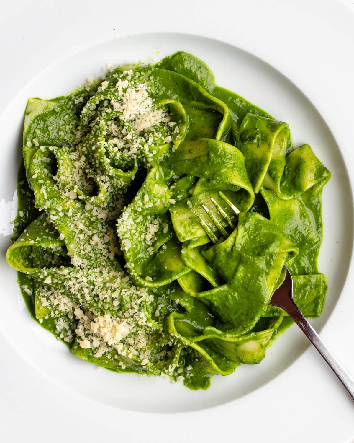 White plate with pappardelle pasta in a cavolo nero green sauce. Fork resting in.