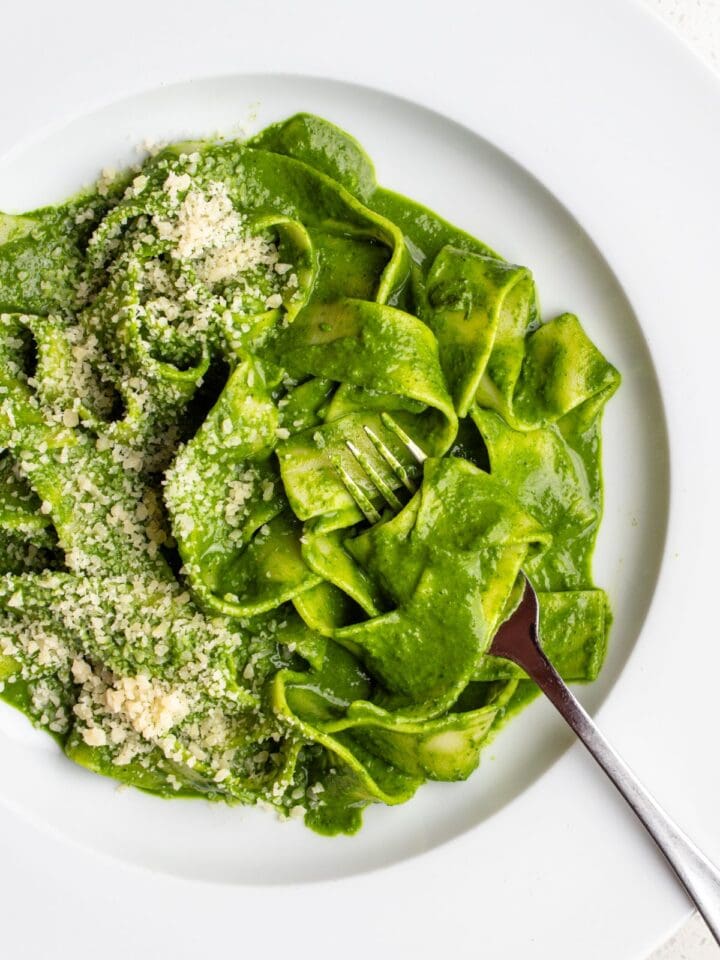 White plate with pappardelle pasta in a cavolo nero green sauce. Fork resting in.