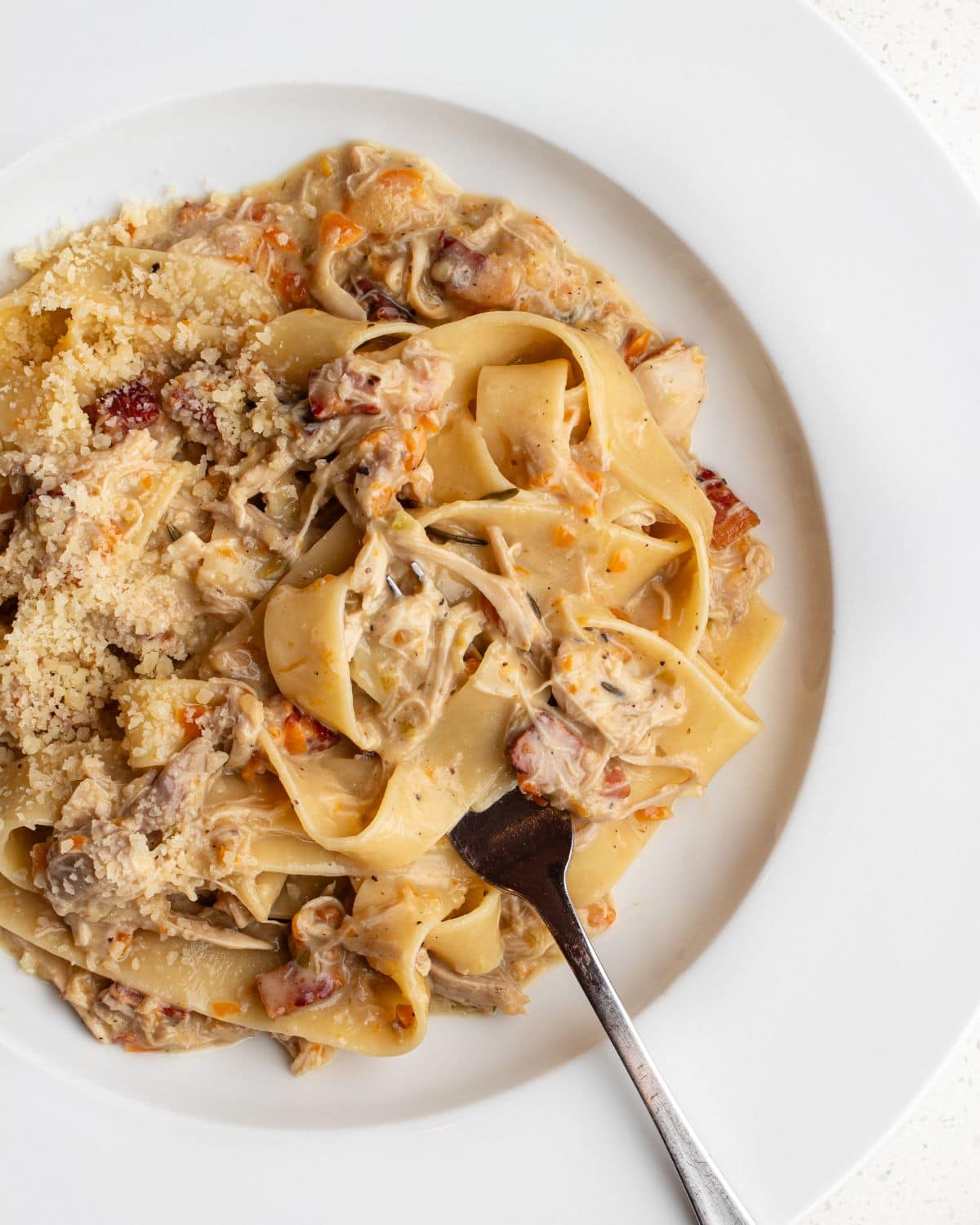 White plate with pappardelle pasta in a chicken ragu. Fork resting.