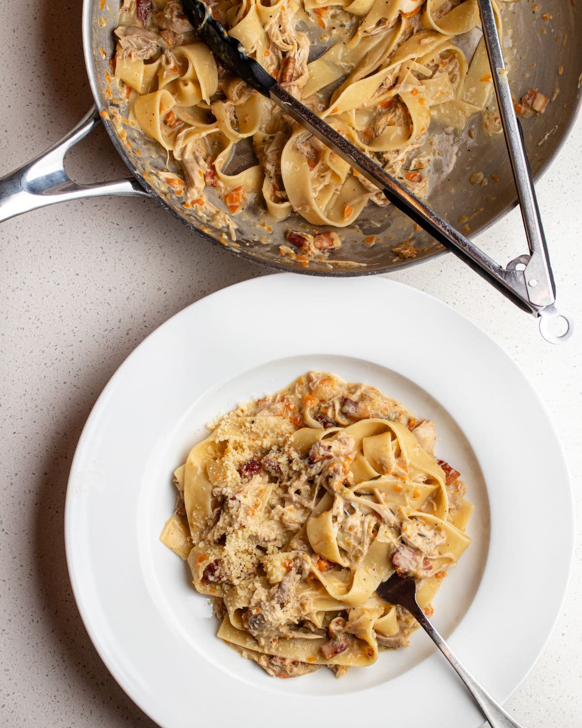 White plate with pappardelle pasta in a chicken ragu. Fork resting. Fry pan above with tongs and remaining ragu.