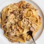 White plate with pappardelle noodles in a chicken ragu. Fork resting into pasta.