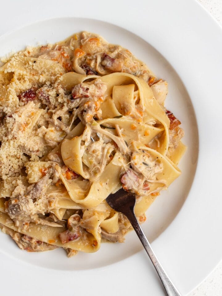 White plate with pappardelle pasta in a chicken ragu. Fork resting.